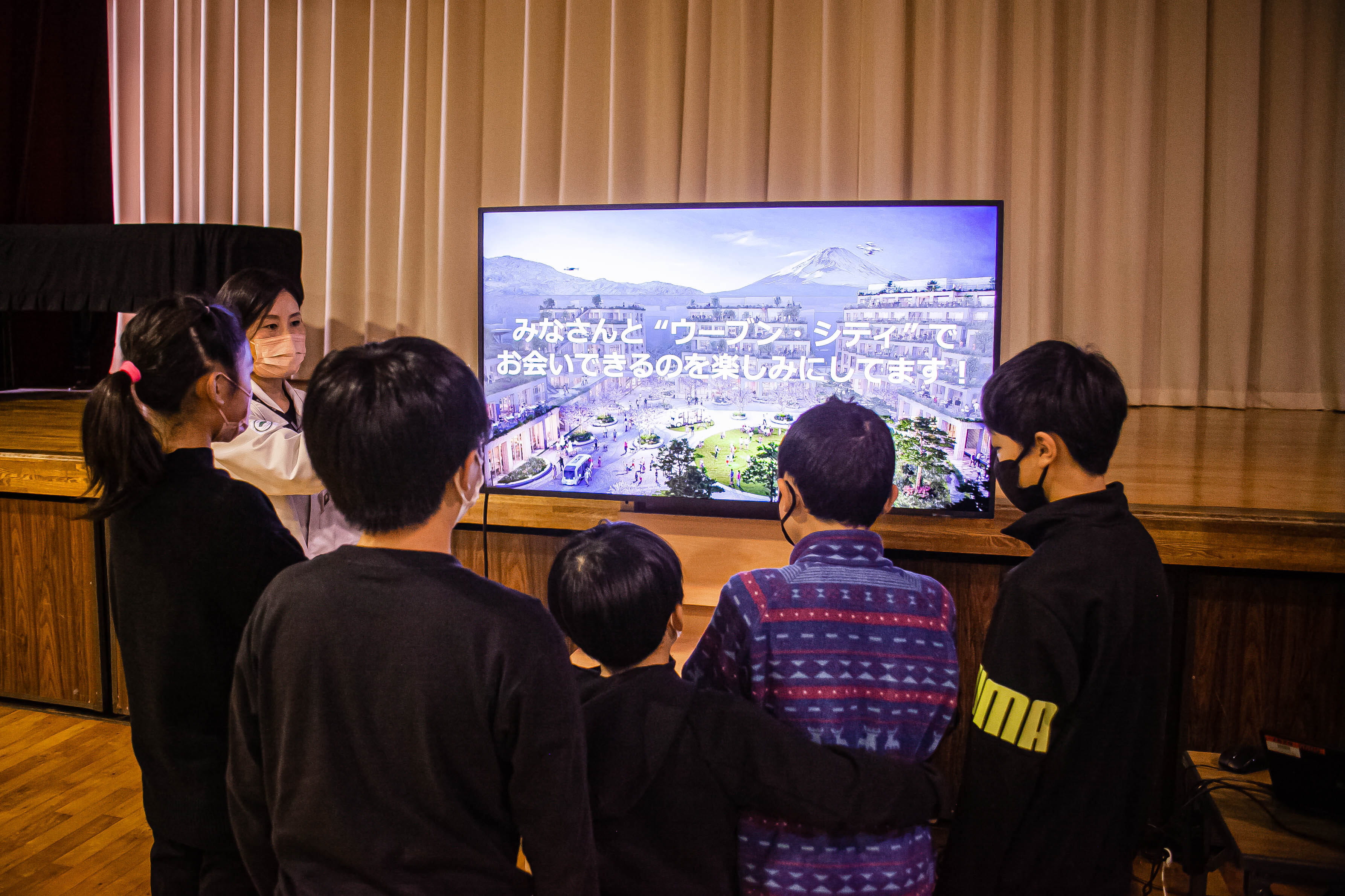 ウーブン・シティを紹介するモニターに集まる生徒の写真