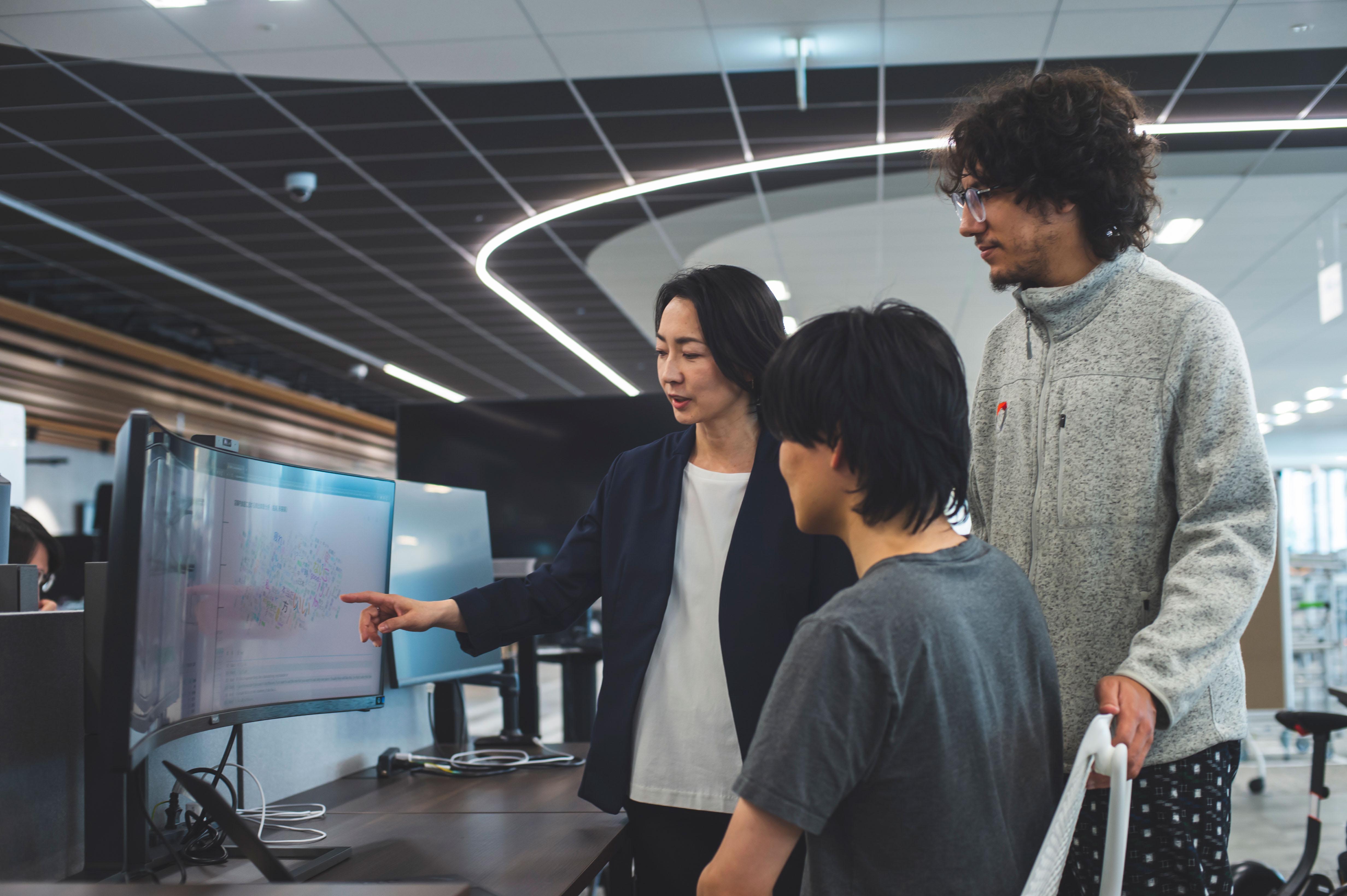 モニターの前に座る男性と、隣で立って話しているウーブン・バイ・トヨタの鈴鹿さんとマルワンさんの様子の写真