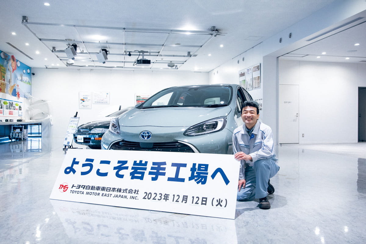 Commemorative photo of Nagatani with the Toyota Motor East Japan Iwate Plant welcome sign and a display vehicle